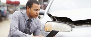 An African-American man making a phone call after being involved in an accident and asking himself is damage covered on rental car if I used credit card.