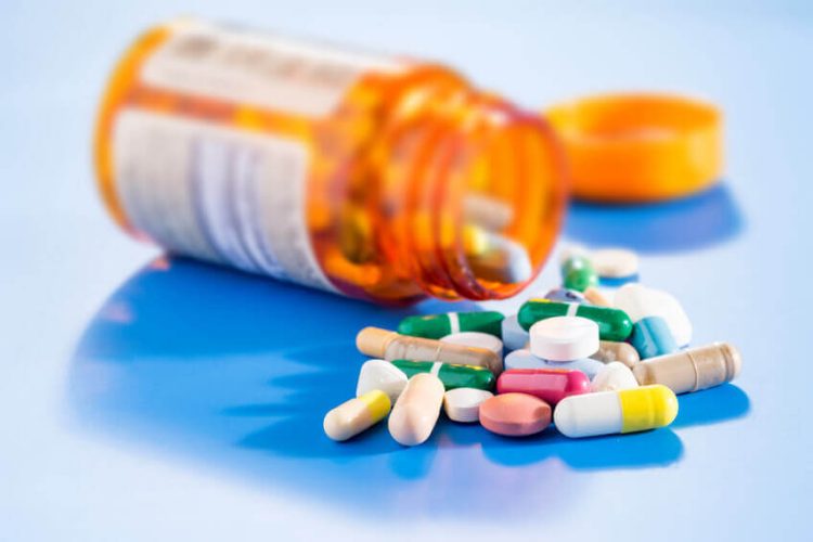 Prescription medicine flask lying on it's side, opened. A pile of different pills and capsules next to it.