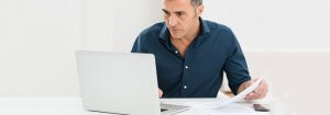 A middle-age man comparing insurance policies and researching on laptop that illustrates how to compare car insurance policies.