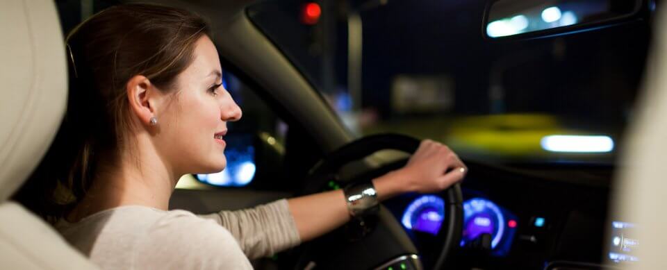 A young, Caucasian woman sitting at the wheel and driving at night illustrates the dangers of driving at night.