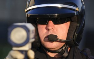 A traffic officer in a helmet holding a radar device to catch drivers while speeding to illustrate how the DMV point system works.