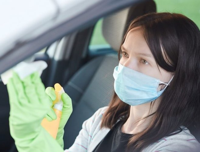 A young, Caucasian woman sanitizing her car with gloves