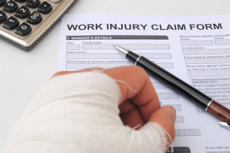 Closeup to a bandaged hand on top of a Work Injury Claim Form. Next to it, a pen also on the form.