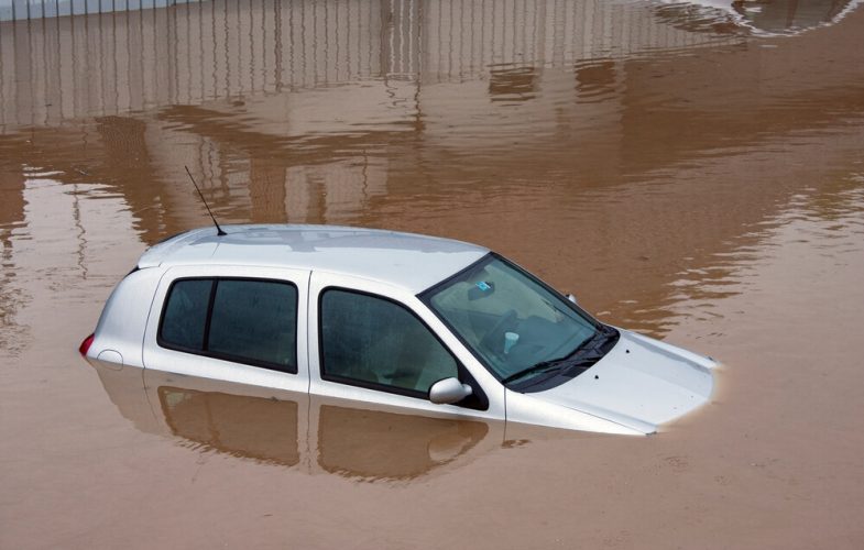 White car submerged up to the windows in brown flood water - cheap car insurance.