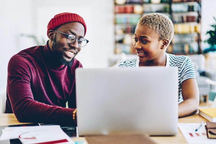 Young Black couple apartment-shopping online on their laptop on a desk.