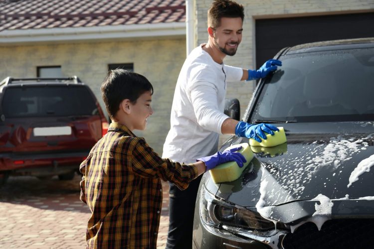 Dad and son washing car at backyard on sunny day