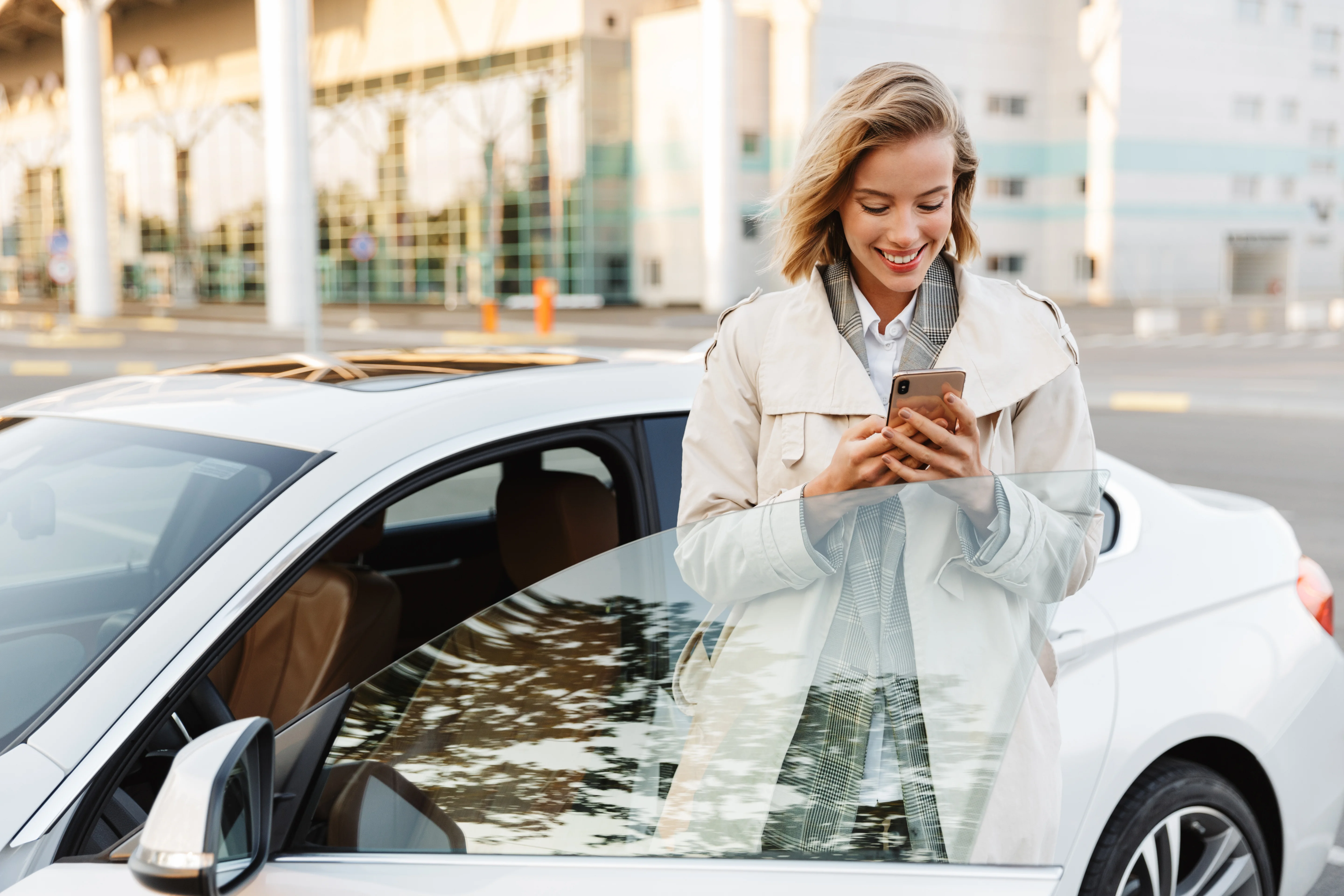Woman smiling and holding her phone while opening the door of her car thinking about getting Auto refinancing