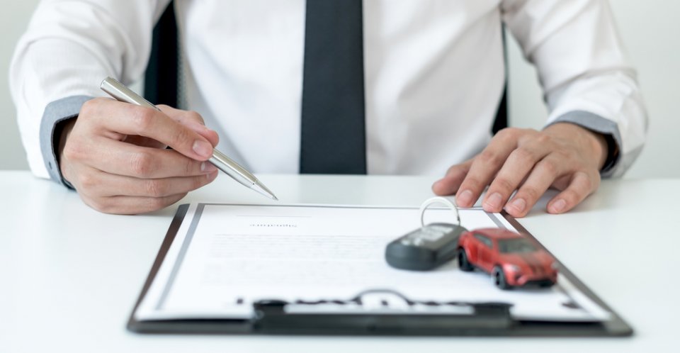 man signing auto insurance paperwork on clipboard