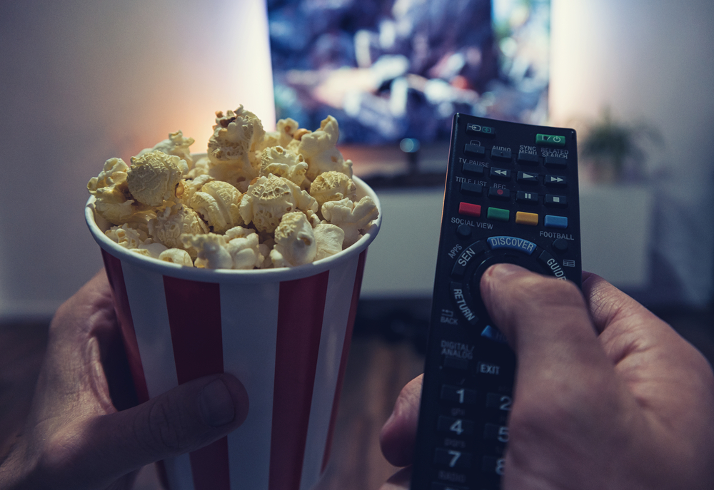 person with remote and popcorn in hand watching a movie