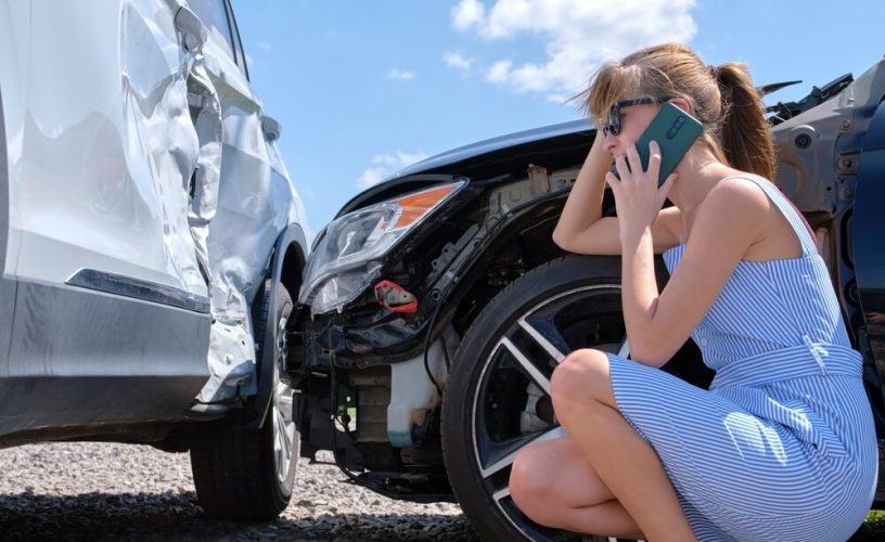 A young woman examines her car while on the phone after a wreck, concept of liability insurance - cheap car insurance.