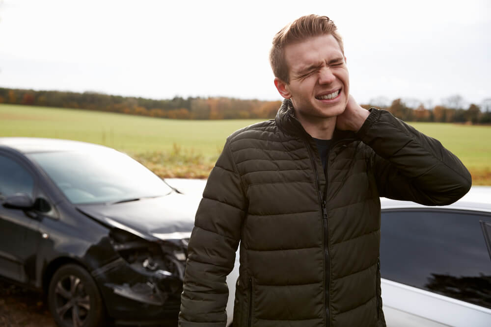 A man grimaces in pain and holds his neck after a car wreck, liability insurance - cheap car insurance.