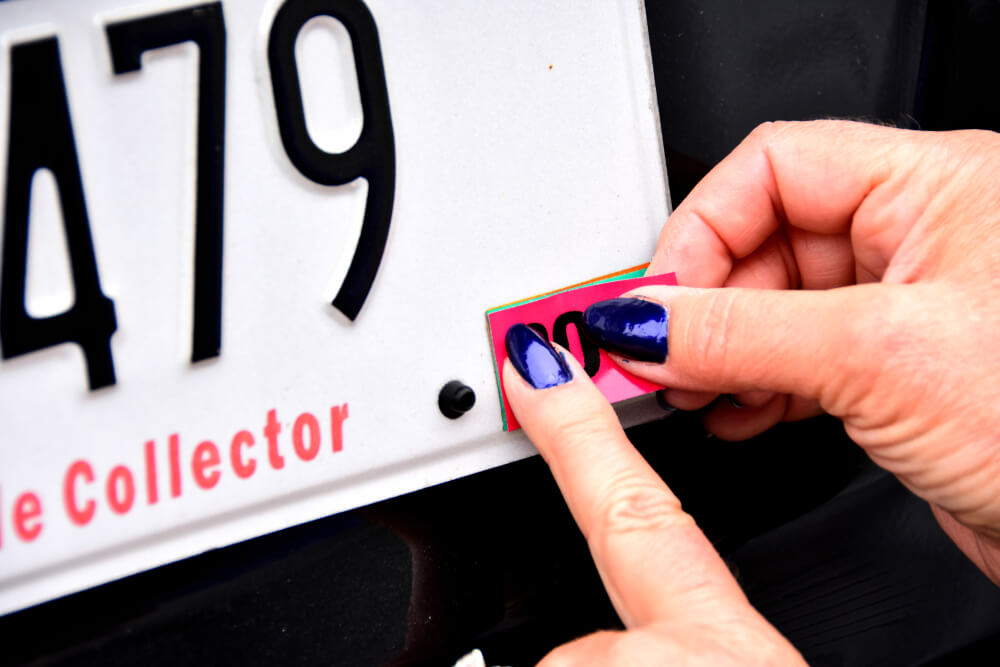 Female fingers and hands applying license plate registration sticker