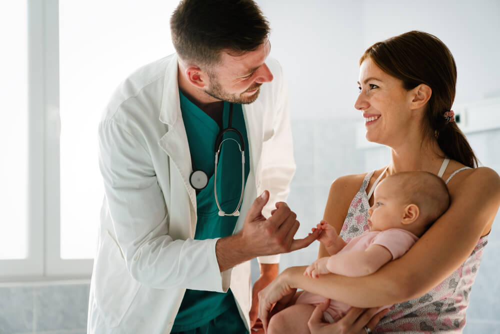 A pediatrician examines a baby who is sitting in her mother's lap - free healthcare information.