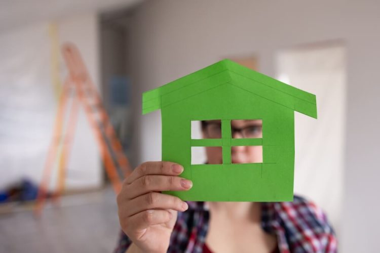 A woman making paper airplanes at home, holding a green paper airplane, while thinking about her homeowners insurance.