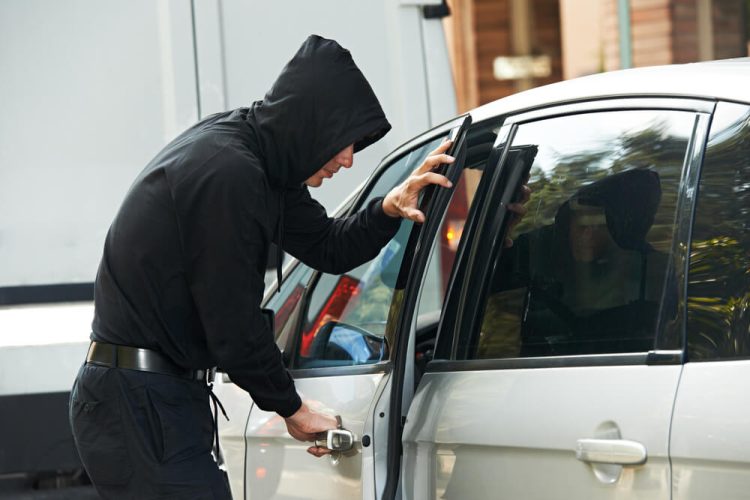 Man in black hoodie breaks into car.