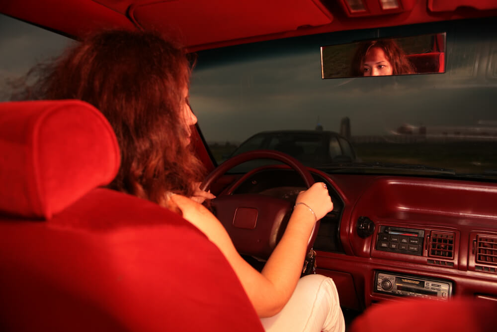 Retro image of a girl driving an older vehicle and looking in the mirror - cheap car insurance.