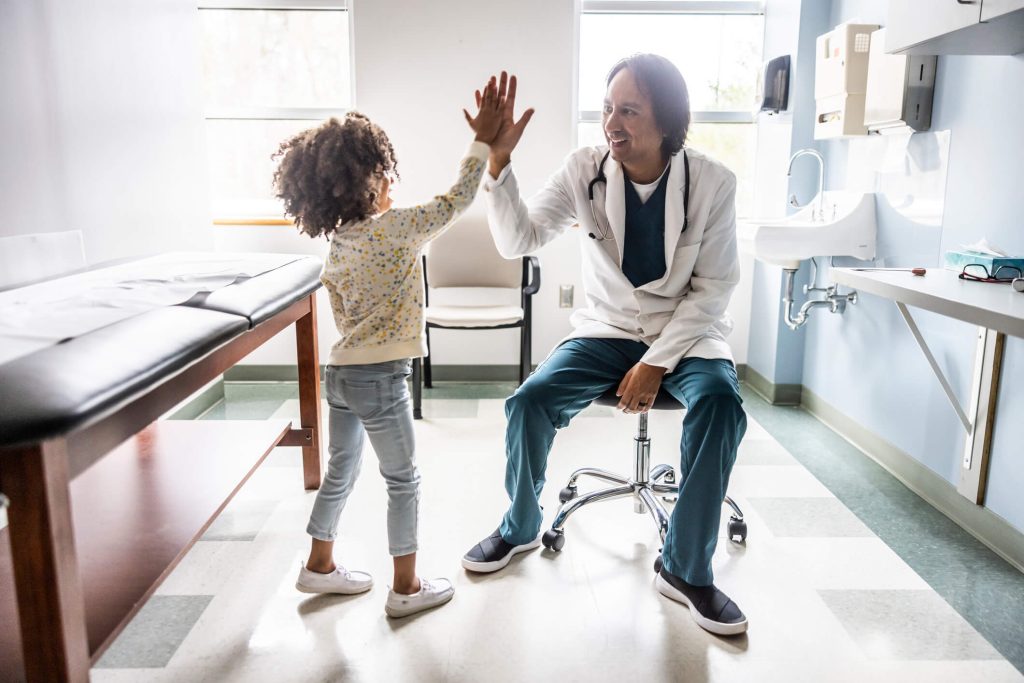 Doctor sitting and high fiving little girl in doctors office.