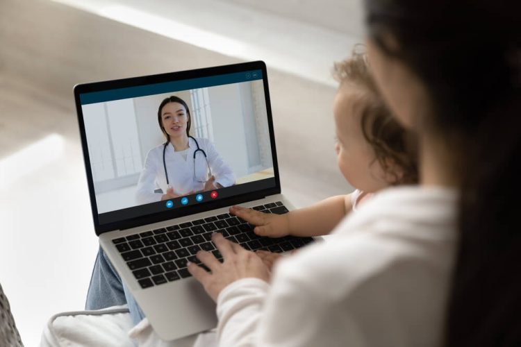 Mom and baby sitting on her lap in a telemedicine appointment.