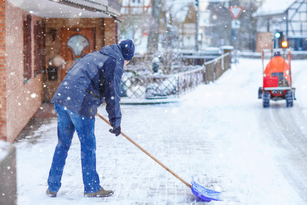 Man with snow shovel cleans sidewalks in winter during snowfall