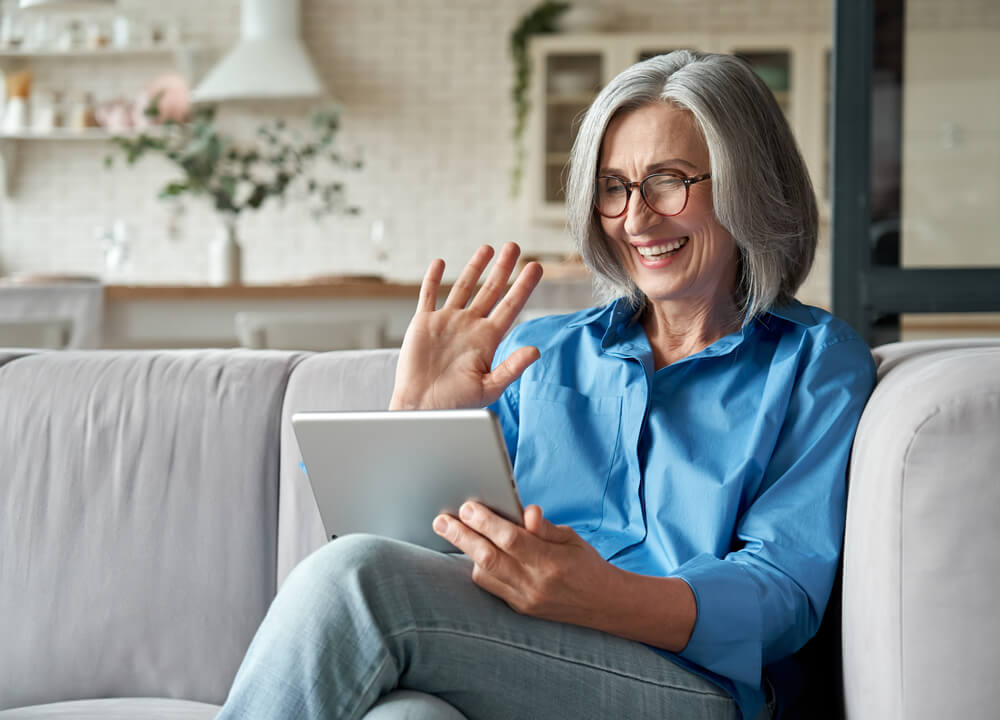 Senior woman discusses her chronic disease management with her doctor on her laptop, sitting on the couch in her home.