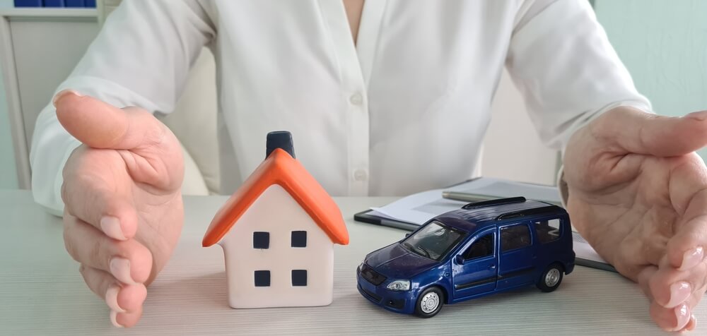 Hands encircling a play house and play car, graphic illustrating the concept of bundling insurance policies - cheap car and home insurance.